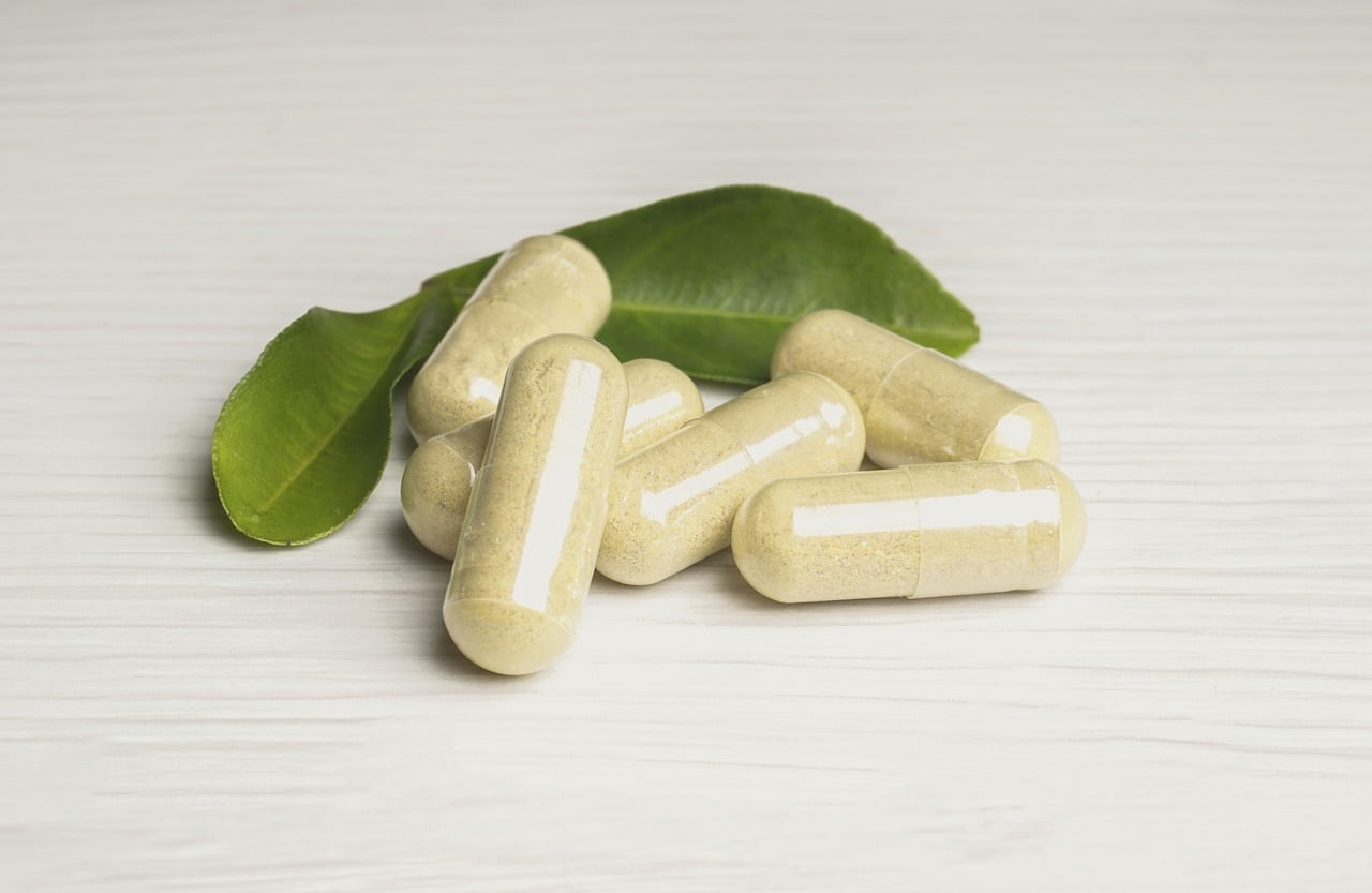 Supplement capsules beside green leaves on a neutral surface