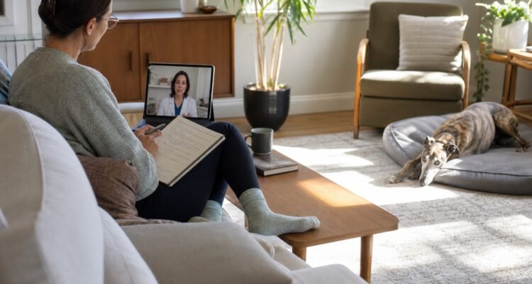 New owner records observations while a brindle Greyhound rests in a quiet home and a veterinarian joins by video.